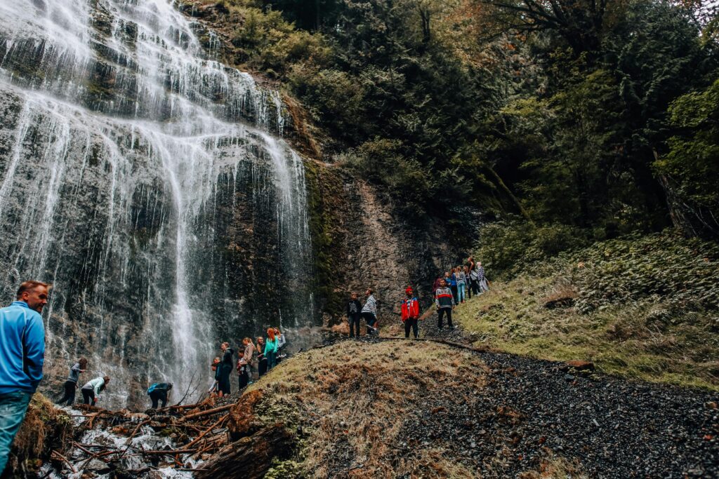 Visitors gather by a majestic waterfall surrounded by lush greenery, capturing the essence of adventure and nature.